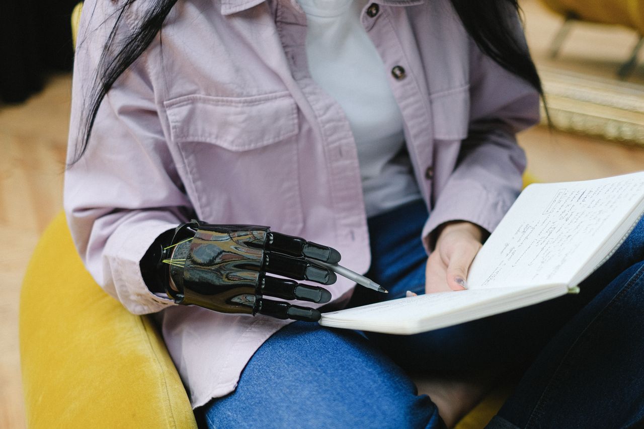 Close-up of a woman with a prosthetic hand writing in a notebook indoors, illustrating technology in daily life.