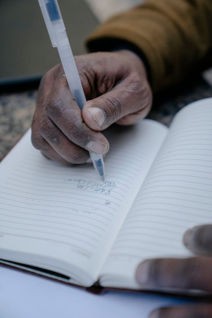7 Edits to Instantly Improve Your Copy An adult hand holding a pen writing in an open notebook.